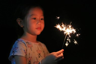 Küçük Asyalı çocuk kız zevk havai fişek oynuyor. Yangın maytap odak.