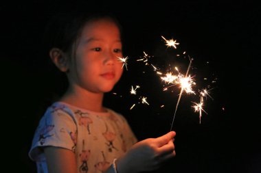 Küçük Asyalı çocuk kız zevk havai fişek oynuyor. Yangın maytap odak.