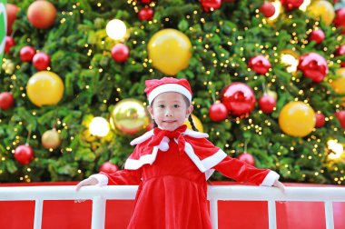 Mutlu sevimli küçük Asyalı çocuk kız Noel ağacı ve arka plan yakınındaki Santa kostüm. Noel kış tatil kavramı.