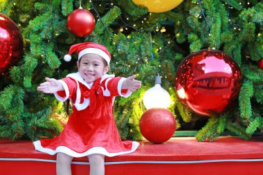 Mutlu sevimli küçük Asyalı çocuk kız Noel ağacı ve arka plan yakınındaki Santa kostüm. Noel kış tatil kavramı.