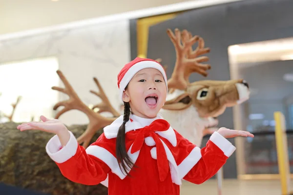 愉快的小女孩在圣诞老人服装礼服在冬天时间反对驯鹿圣诞节背景 圣诞快乐 新年快乐 — 图库照片