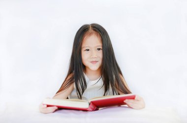 Küçük Asyalı çocuk kızla yastığın beyaz arka plan üzerinde yatan ciltli kitap okuma.
