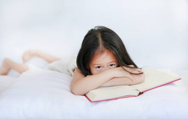 Sevimli küçük Asyalı çocuk kız beyaz zemin üzerine yastık üzerinde ciltli kitap ile yalan.