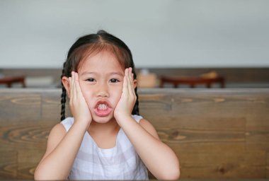 Kameraya bakarak ahşap masanın üzerinde yatan ifade komik surat ile küçük Asyalı kız.