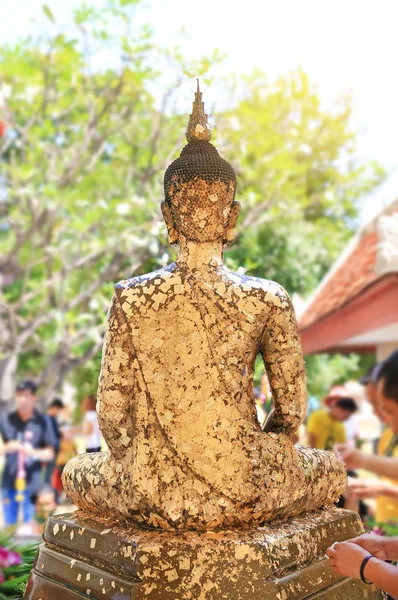 People sticking the gold foil sheet on back Buddha statue for respect.