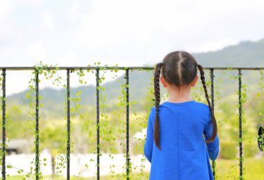 Balkon ayakta ve doğaya bakan küçük Asisn çocuk kız arkadan görünüş.