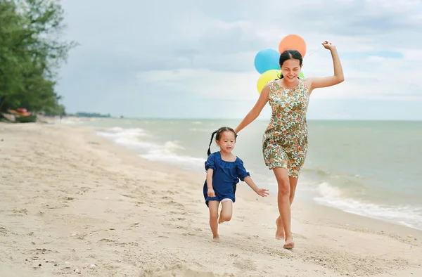 Portrait of Mother and daughter running on beach with colorful balloons in mother hand.