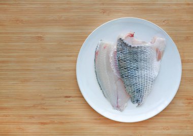 Ham tilapia balık fileto ahşap tahta arka plan kopya alanı ile beyaz plaka üzerinde.