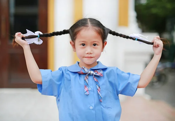 微笑的小亚洲女孩在学校制服拿着她的两根绑马尾毛 — 图库照片