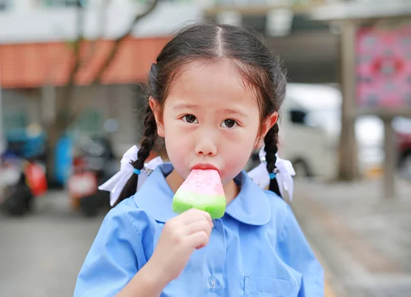 可爱的亚洲小女孩穿校服在公园里吸吮或吃冰淇淋 — 图库照片