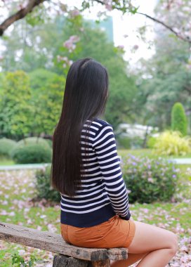 Arka görünümü Asyalı kadın bakan ile açık bahçe ahşap bankta oturmuş.