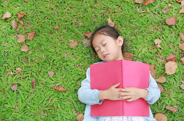 夏の庭の乾燥した葉と緑の草の上に横たわる本載って女の子 — ストック写真