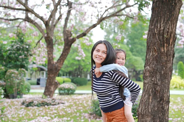 周りに完全に秋のピンク花と庭で彼女の小さな子の女の子を運ぶ母の笑みを浮かべてください 幸せな愛情のある家族 — ストック写真