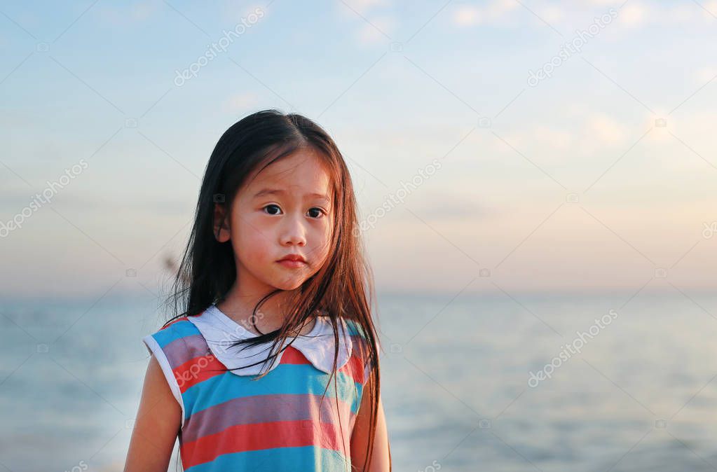 Peaceful little child girl standing on beach at sunset light with looking camera.