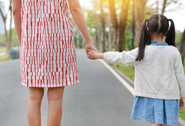 Yakın çekim anne ve kızı açık doğa bahçesinde el ele tutuşuyor. Geri görünüm.