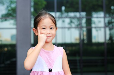 Küçük gülümseme ile onu işaret parmağı yukarı işaret Asya küçük kız duruş.