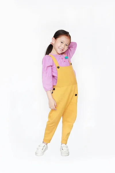 Smiling little Asian kid girl in pink-yellow dungarees poses tou — Stock Photo, Image