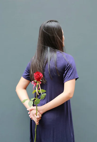 Portrait of Asian woman hiding red roses behind her back. Rear view.