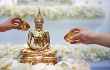 Water blessing ceremony for Songkran Festival or Thai New Year. People paying respects to a statue of Buddha by pouring water onto it. clipart