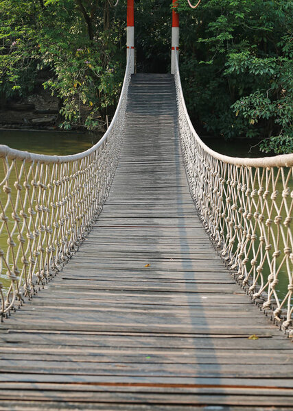 Wooden rope suspension bridge for walk crossing river.