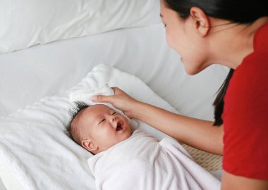 Anne banyodan sonra yatakta yatan havlu küçük bebek çocuk gülümseyen için vücut kuru ovmak.