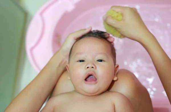 Six month old Asian infant boy having a bath by mother.