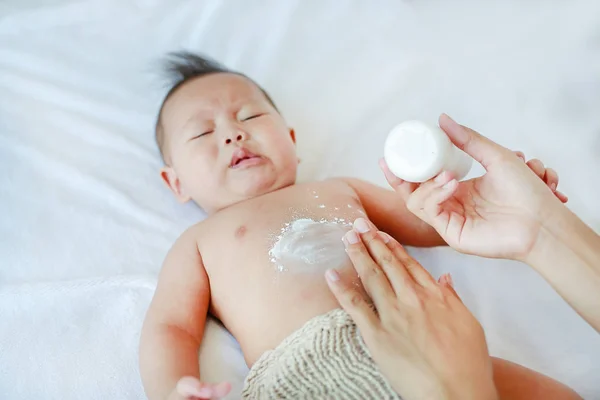 Mother applying Talcum powder to her infant baby boy on bed after bath.