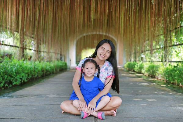 Portrait of Asian mother and daughter sitting under beautiful root of Banyan tree.