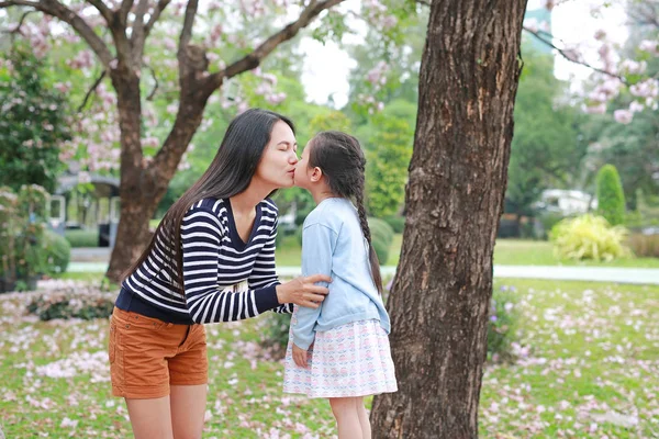 アジアの母親は 屋外の周りに完全にピンクの花と庭で彼女の娘にキス — ストック写真