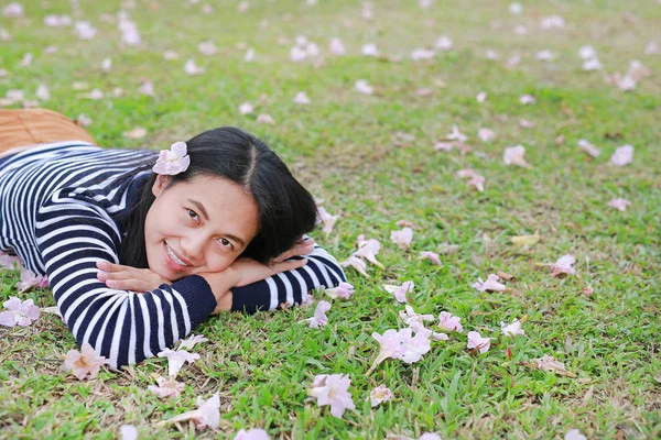 Beautiful young Asian woman lying on green field with fully fall pink flower in the garden outdoor.