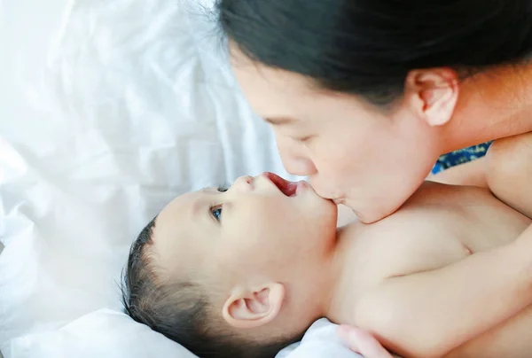 Close-up Asian mom playing and kissing her little baby boy on the bed.