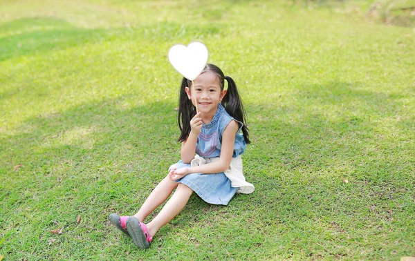 Adorable Niña Asiática Sosteniendo Etiqueta Corazón Blanco Sentado Césped Verde —  Fotos de Stock