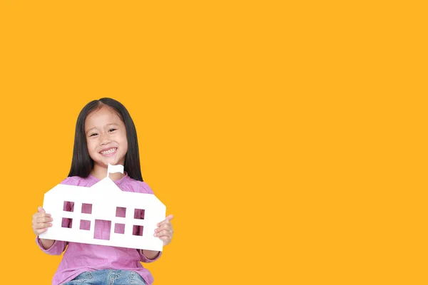 Happy little Asian child girl holding mock-up paper school isolated on yellow background with copy space. Education and back to school concept.