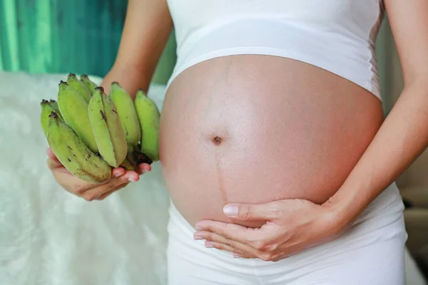 怀孕的妇女站在房间里 抱着一堆绿色的香蕉在她的肚子上 — 图库照片