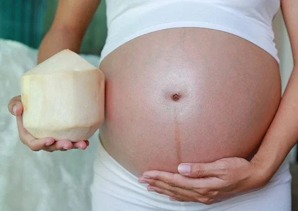 怀孕妇女抱着椰子在她的肚子上 — 图库照片