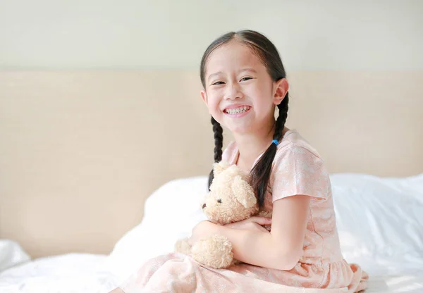 Sorrindo Asiático Menina Pequena Abraçar Ursinho Pelúcia Sentado Cama Casa — Fotografia de Stock