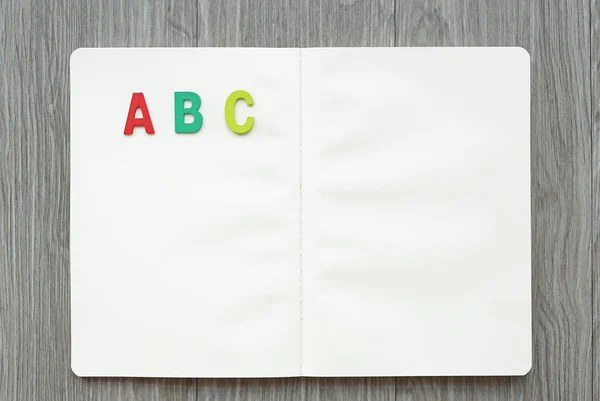 Opened blank book with letters ABC on wood table. Education concept.