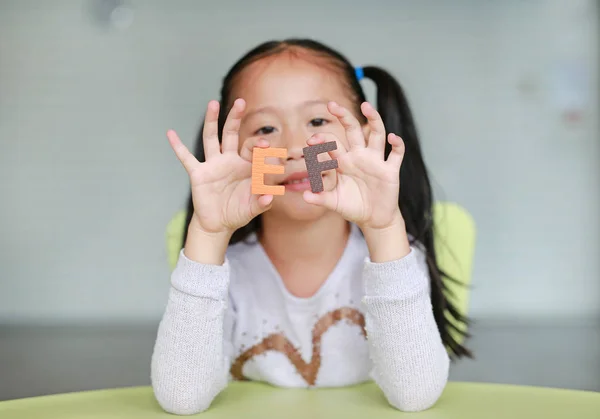 Adorable little Asian child girl holding alphabet EF (Executive Functions) text on her face. Education concept.