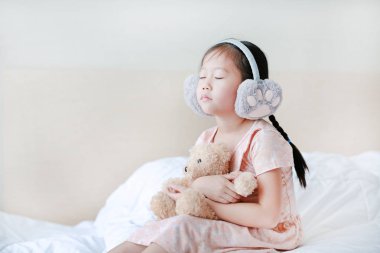 Kapalı gözleri küçük Asya çocuk kız kış earmuffs giyen ve 