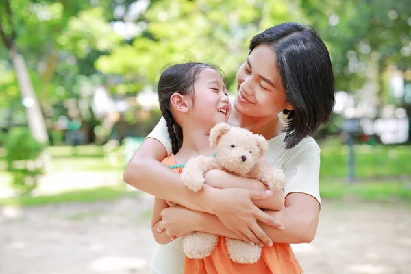 幸福的亚洲母亲拥抱女儿和拥抱泰迪熊娃娃在花园里的肖像 妈妈和孩子女孩与爱和关系的概念 — 图库照片