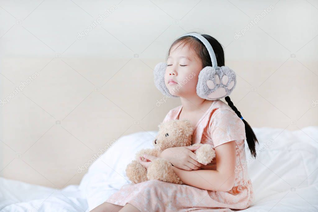 Closed eyes little Asian child girl wearing winter earmuffs and 