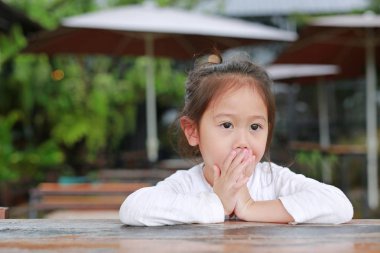 Huzurlu küçük Asyalı çocuk kız ahşap masada yatan dışarı bakıyor.