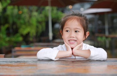 Bakan ile ahşap masanın üzerinde yatan gülümseyen küçük Asyalı çocuk kız.