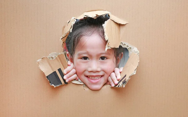 微笑的亚洲小女孩看着通过洞纸板与复制空间周围 — 图库照片