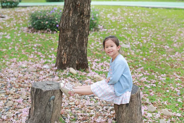 Glückliches Kleines Mädchen Sitzt Auf Holzstämmen Gegen Fallende Rosa Blume — Stockfoto