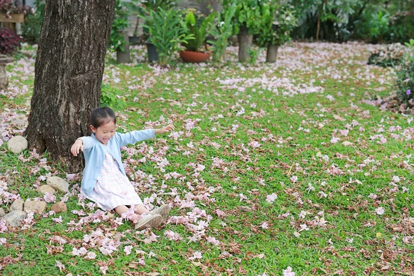 มเด กสาวเอเช ยเล งบนหญ ยวภายใต นไม ดอกไม ชมพ ลดลงในสวน — ภาพถ่ายสต็อก