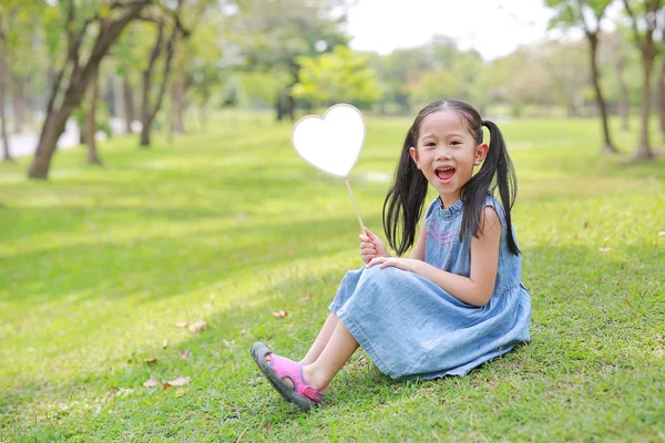 Lächelndes Kleines Asiatisches Mädchen Mit Leerem Herzetikett Auf Grünem Gras — Stockfoto