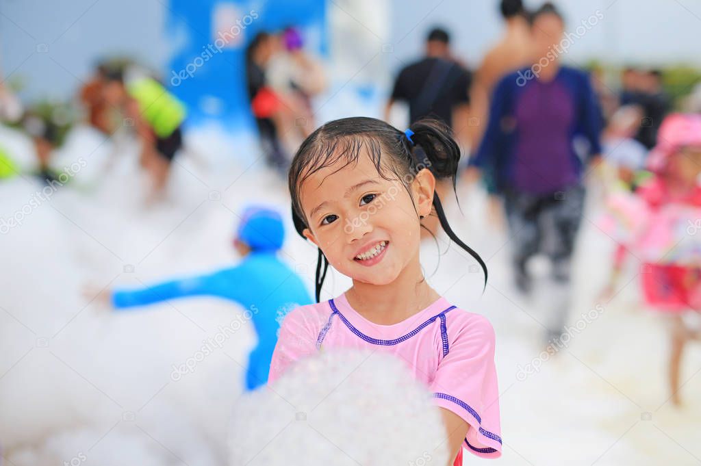 Portraits of happy little Asian child girl smiling having fun in Foam Party at the pool outdoor.