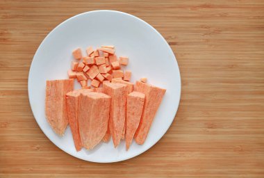 Kopya alanı ile ahşap tahta arka plan üzerinde beyaz plaka içinde çiğ soyulmuş ve doğranmış tatlı patates.