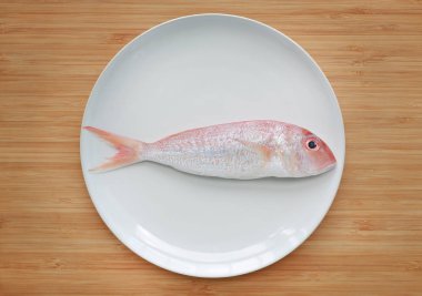 Taze süslü threadfin çipura ahşap tahta arka plan beyaz plaka üzerinde.